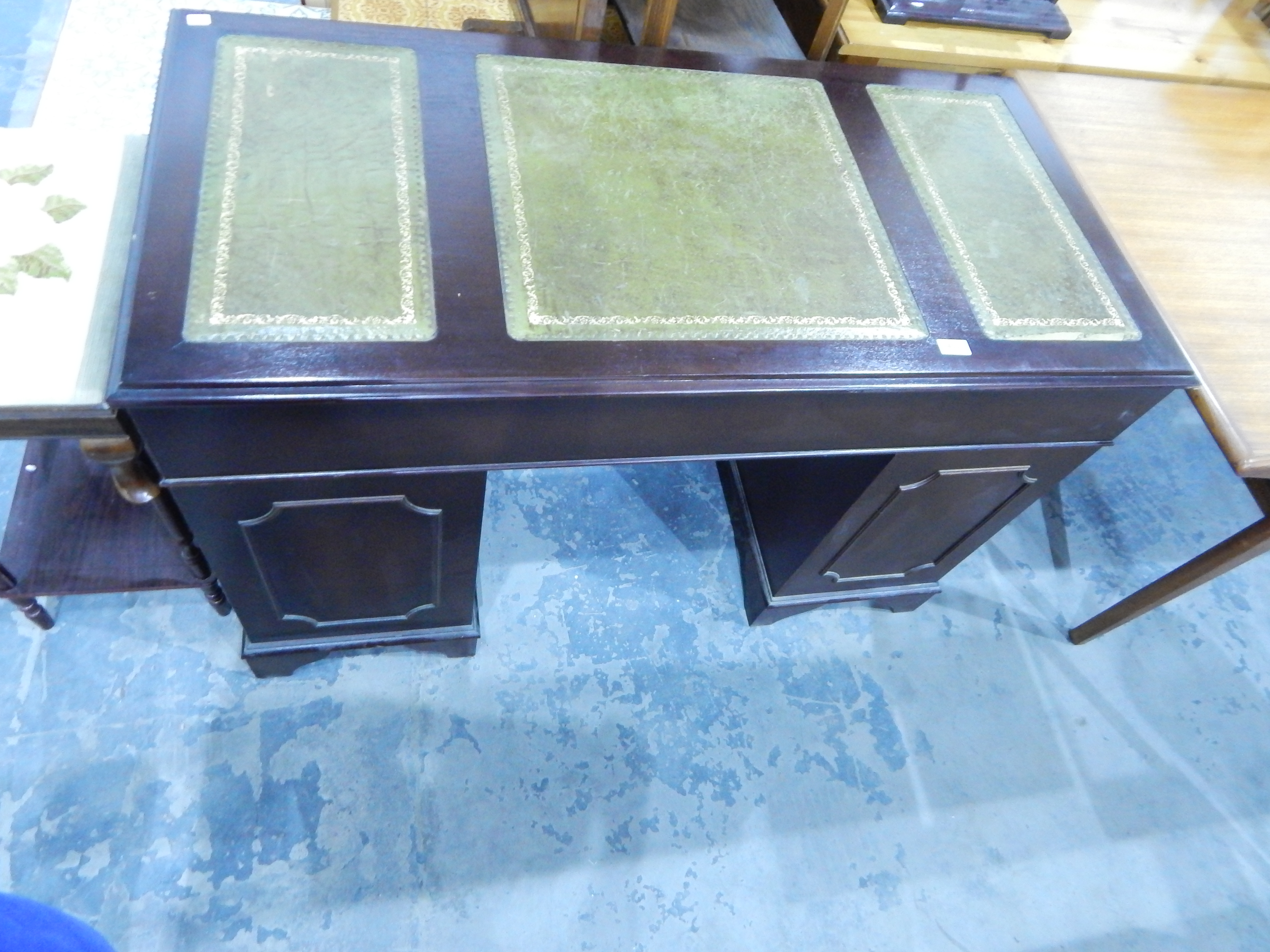 A mahogany finish kneehole pedestal desk, the top inset three tooled leather panels,