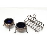 A pair of Georgian silver circular salts on three legs and a silver six-division toast rack,