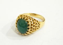 A gold-coloured ring with central green oval cabochon, with pierced mount,