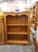 A pine open-fronted bookcase with serpentine skirt, three open shelves, on shaped block plinth,