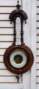 A stained walnut barometer having turned finial to the carved arch above the thermometer,