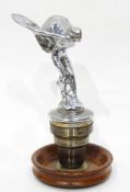 A Rolls Royce Spirit of Ecstasy chrome car mascot now mounted on a circular wooden base,