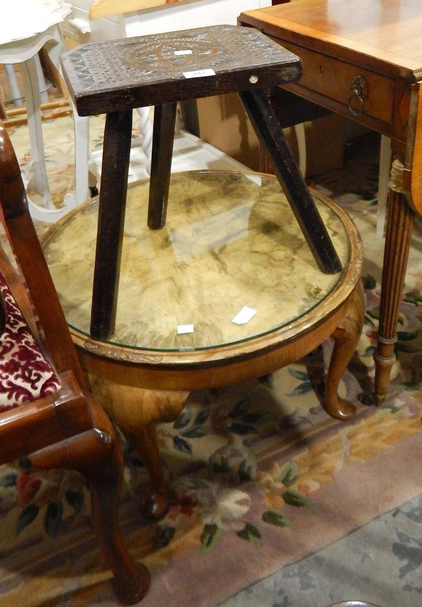 A carved oak three-legged stool and a circular mahogany coffee table with inset glass top,