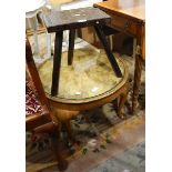 A carved oak three-legged stool and a circular mahogany coffee table with inset glass top,