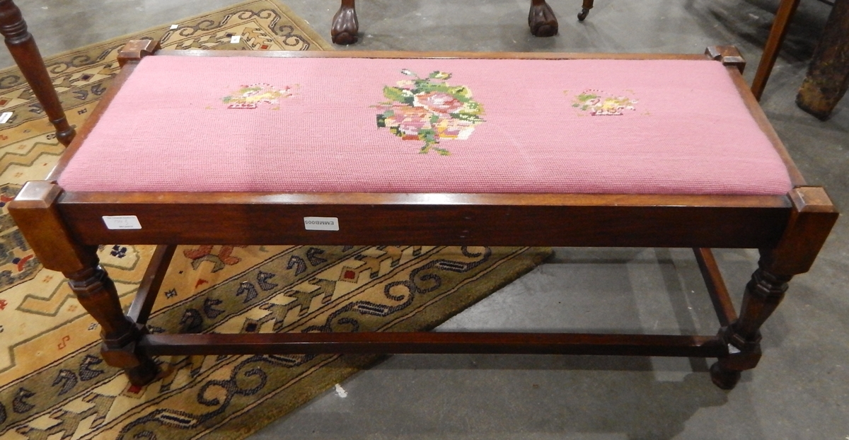 A mahogany long stool with needlework upholstered top, on faceted legs united by stretchers,