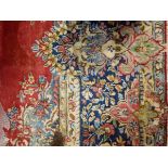 Persian wool carpet with red ground, floral arabesque decoration, blue borders,
