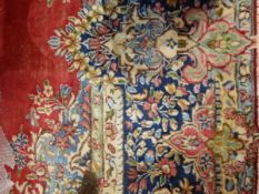 Persian wool carpet with red ground, floral arabesque decoration, blue borders,