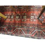 A fine North East Persian Meshad Belouch rug with repeating floral pots on a rouge field within