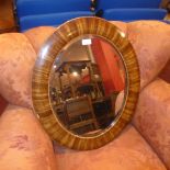 A 20th Century looking glass with oval bevelled plate in an inlaid mahogany frame