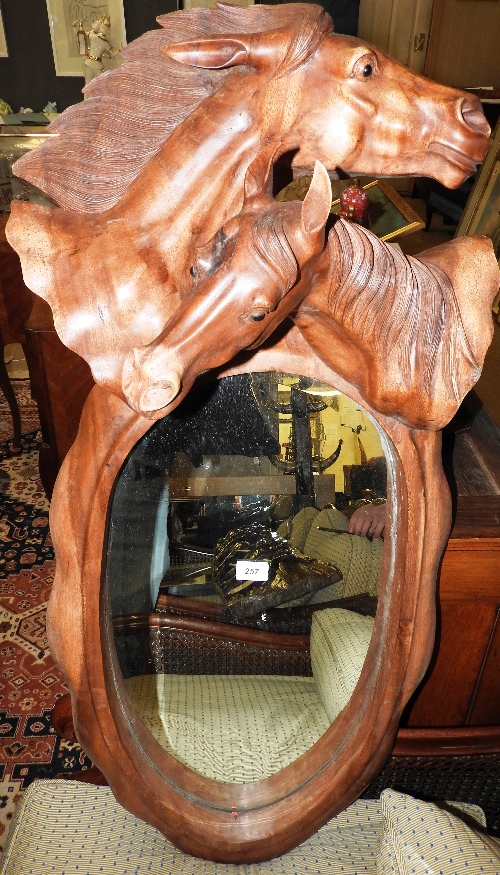 A 20th century oval wall mirror within an ornately carved wooden frame with a crest of two horse