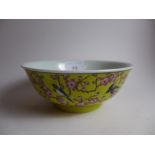 A Chinese famille rose bowl decorated with birds amongst blossom on a yellow ground with a six