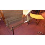 A retro teak Uniflex stool with yellow upholstery and a glass top coffee table raised on black