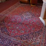 A central Persian Keshan carpet with petal medallion and palmettes on a rouge field framed by a