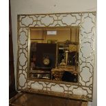 A contemporary designer wall mirror, the square bevelled plate, within pierced gilt metal frame,