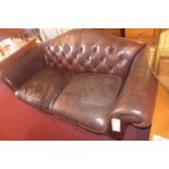 A Laura Ashley two seater sofa upholstered in buttoned brown leather and raised on turned supports