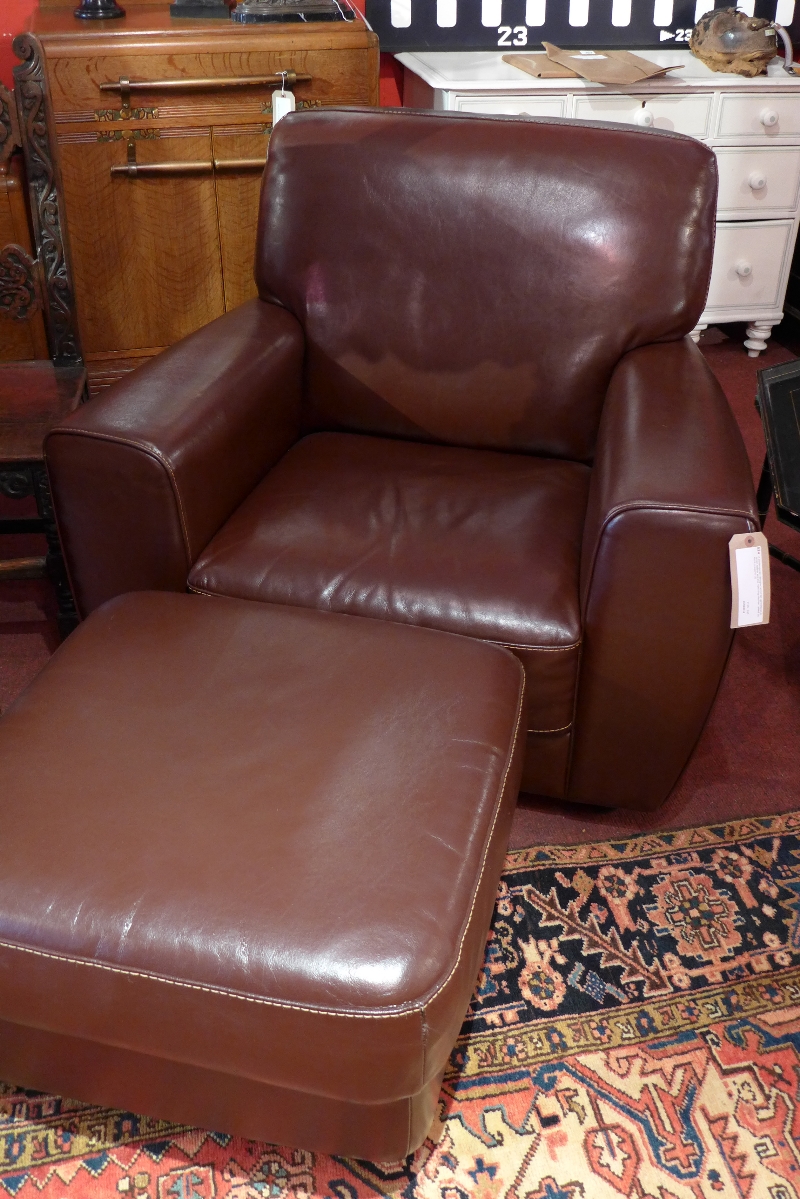 A contemporary designer armchair upholstered in brown leather and the matching ottoman raised on