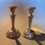 A pair of silver plated candlesticks having ornate detail in relief.