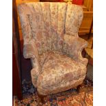 A 20th Century mahogany wing back armchair upholstered in floral fabric and raised on cabriole