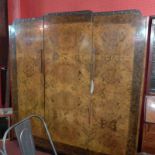 An Art Deco carved burr walnut triple wardrobe fitted three panel doors enclosing hanging space.