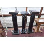 A pair of ebonised column plinths with inset rouge marble tops together with another similar of