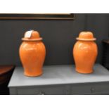 A pair of bulbous form orange vases with lids