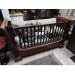 A contemporary designer mahogany sleigh style cot bed, by Simon horn having slatted sides,