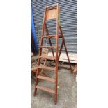 A tall wooden A-frame ladder with flip-down tray