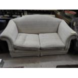 A three seater camel back sofa upholstered in beige fabric and scroll arms