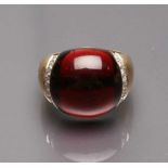 Damenring. 750/000 GG, brutto 10,9 g. Großes, rotes (Granat-?)Cabochon (best.), flankiert von 16