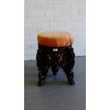 A carved teak stool of circular form with an upholstered top raised on Antelope head carved supports