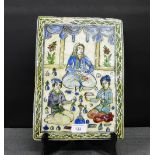 A Persian rectangular glazed tile, likely 19th century, painted with three kneeling figures within a