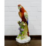 A porcelain figure of a parrot, model perched upon a tree stump on a naturalistic rocky base, has