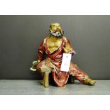 A Japanese red glazed figure of an axe man, modelled seated on a trestle stool, 28cm high