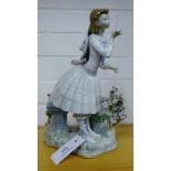 A Lladro porcelain figure of a girl standing by a stone bench and flowering tree stump, on a