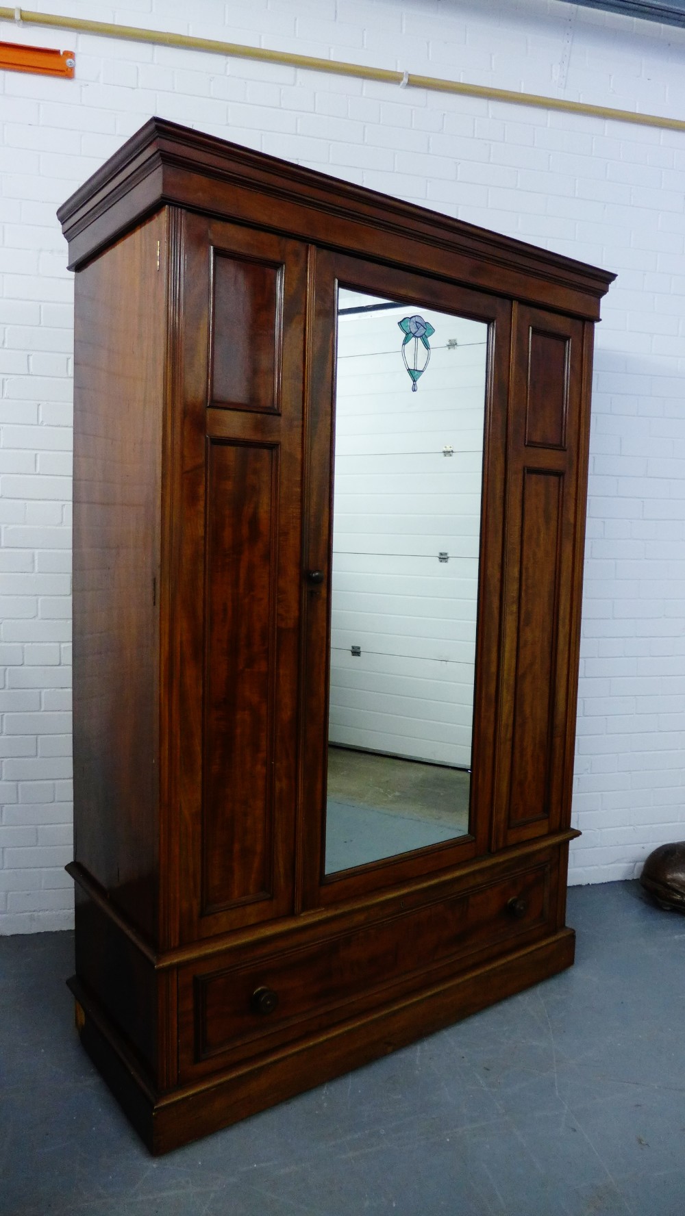 A mahogany wardrobe, the pediment top over a central mirrored panel door opening to reveal a