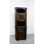 A dark oak Ercol style corner cabinet with a glazed cupboard door above single frieze drawer and