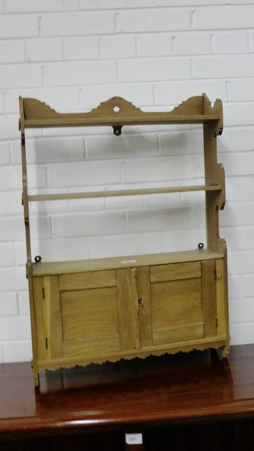 A country pine wall rack, the shaped top over two open shelves and a pair of panel cupboard doors to