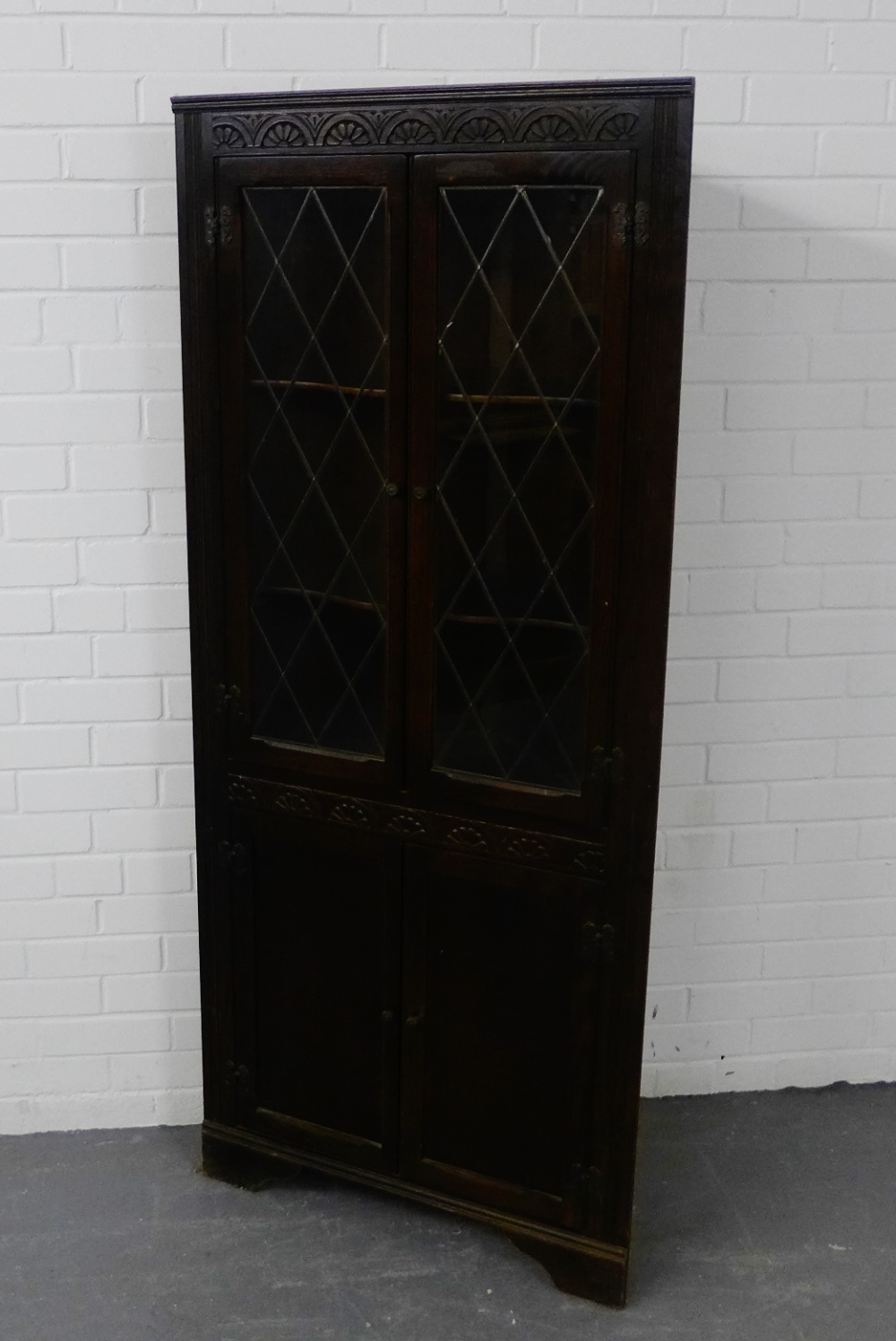 A dark oak corner cabinet with a carved frieze over a pair of astragal glazed doors and cupboard