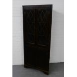 A dark oak corner cabinet with a carved frieze over a pair of astragal glazed doors and cupboard