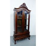 A stained hardwood armoire cabinet, the domed top surmounted by a carved scrolling frieze over