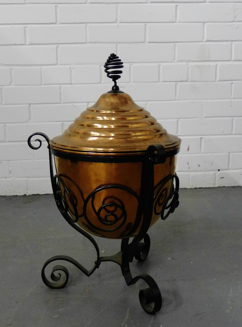 An Arts and Crafts copper coal bucket in a black iron scrolled support, 55cm