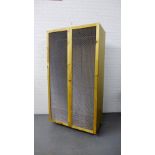 A contemporary pine wardrobe with twin doors with wire mesh fronts, on wheels, 190 x 102cm