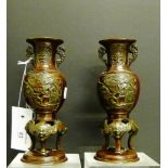 A pair of twin handled bronze vases with birds and foliage panels on tripod supports and circular