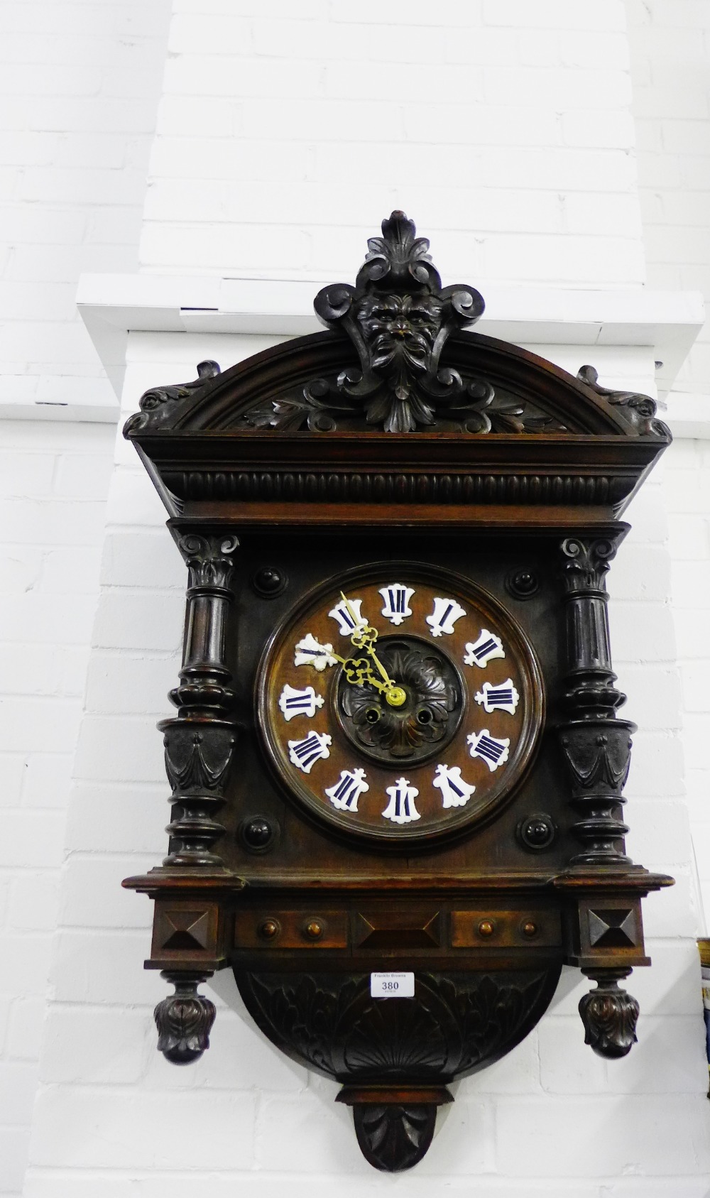 A black forest style wall clock with a carved pediment top with a green man motif to centre over a