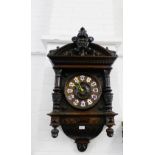 A black forest style wall clock with a carved pediment top with a green man motif to centre over a