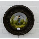 An enamel plate painted with a female figure to centre all contained within a bronzed metal