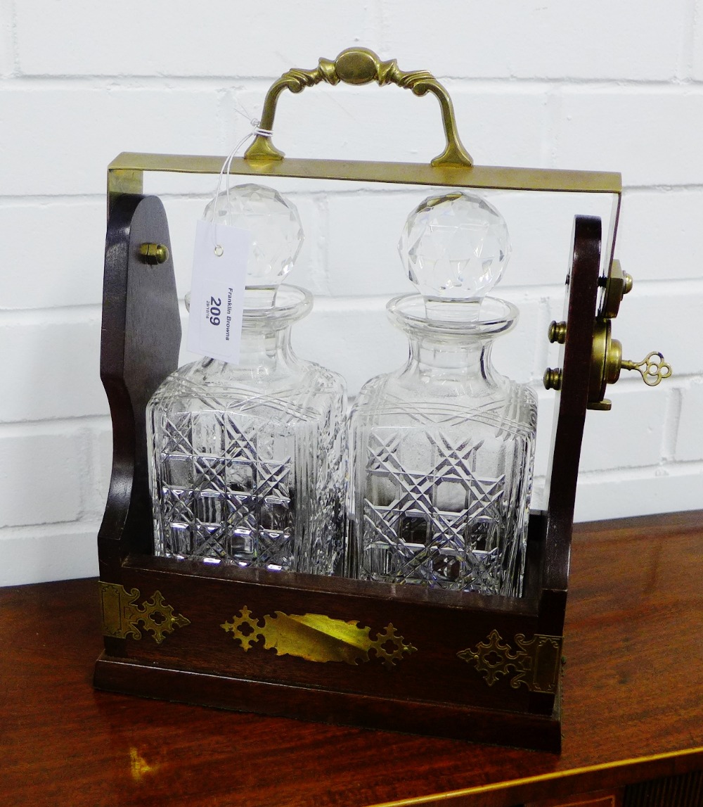 A Tantalus with brass handles and mounts, containing a pair of cut glass decanters and stoppers,