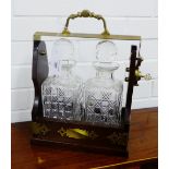 A Tantalus with brass handles and mounts, containing a pair of cut glass decanters and stoppers,