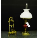 A brass table oil lamp with a cranberry glass well and a white opaque glass shade, together with a