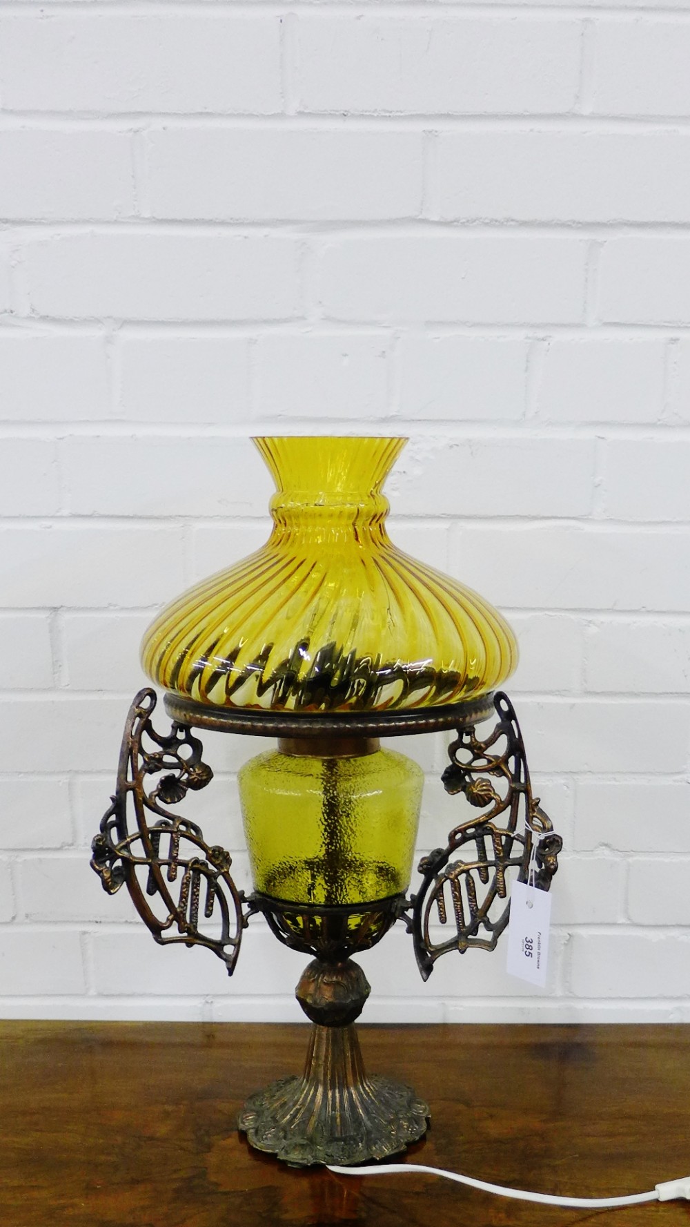 A coppered metal table lamp base with amber glass well and shade